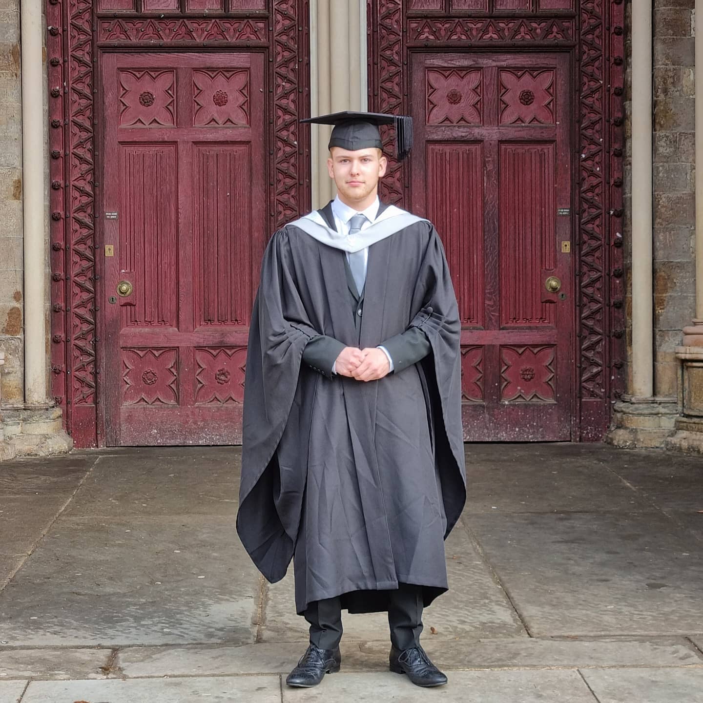 Photo of Robert standing in front of St Albans Cathedral in Graduation robes